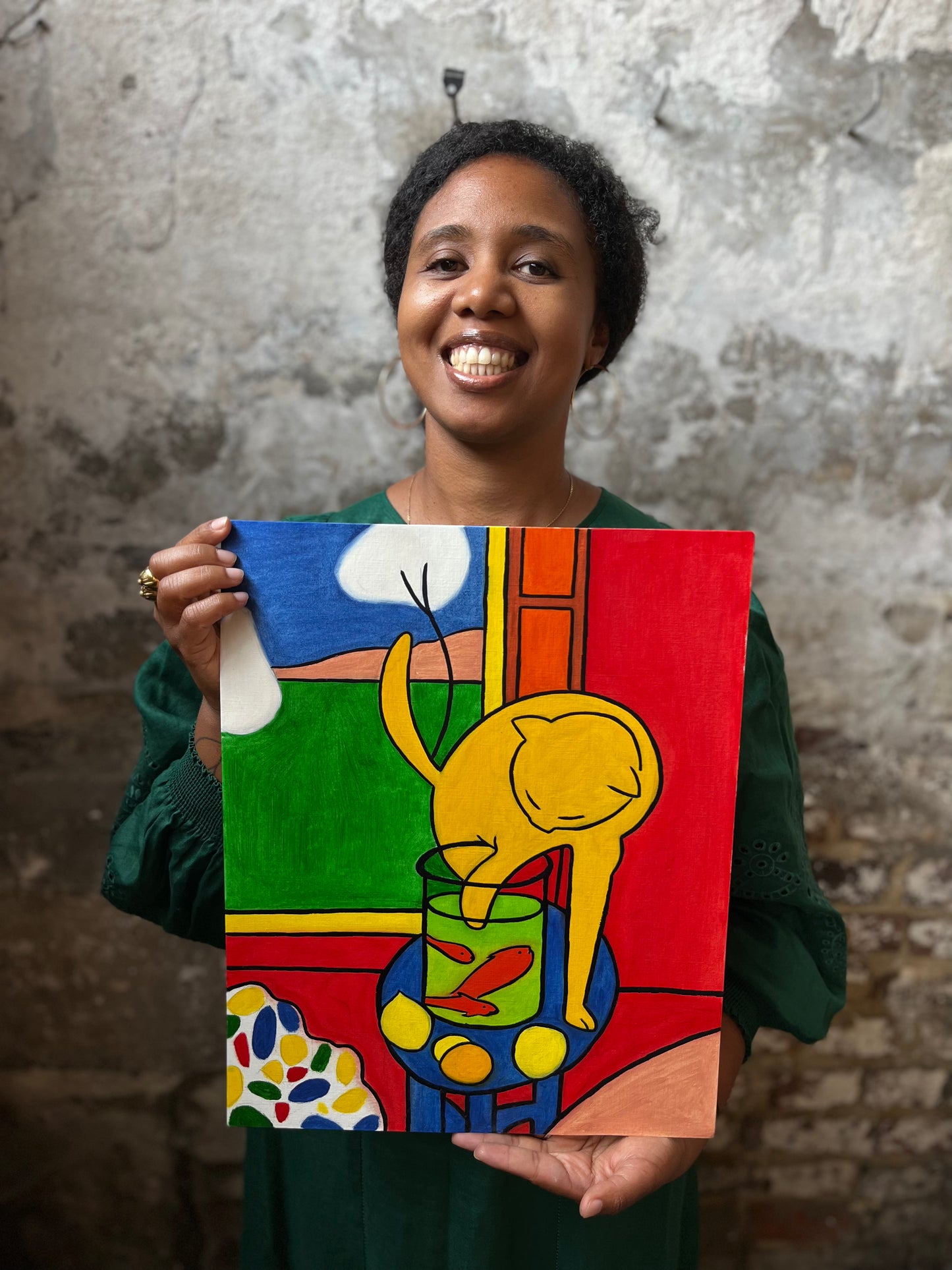 A black woman holding a print of a Matisse oil painting of a yellow cat trying to catch red fish in front of an open window