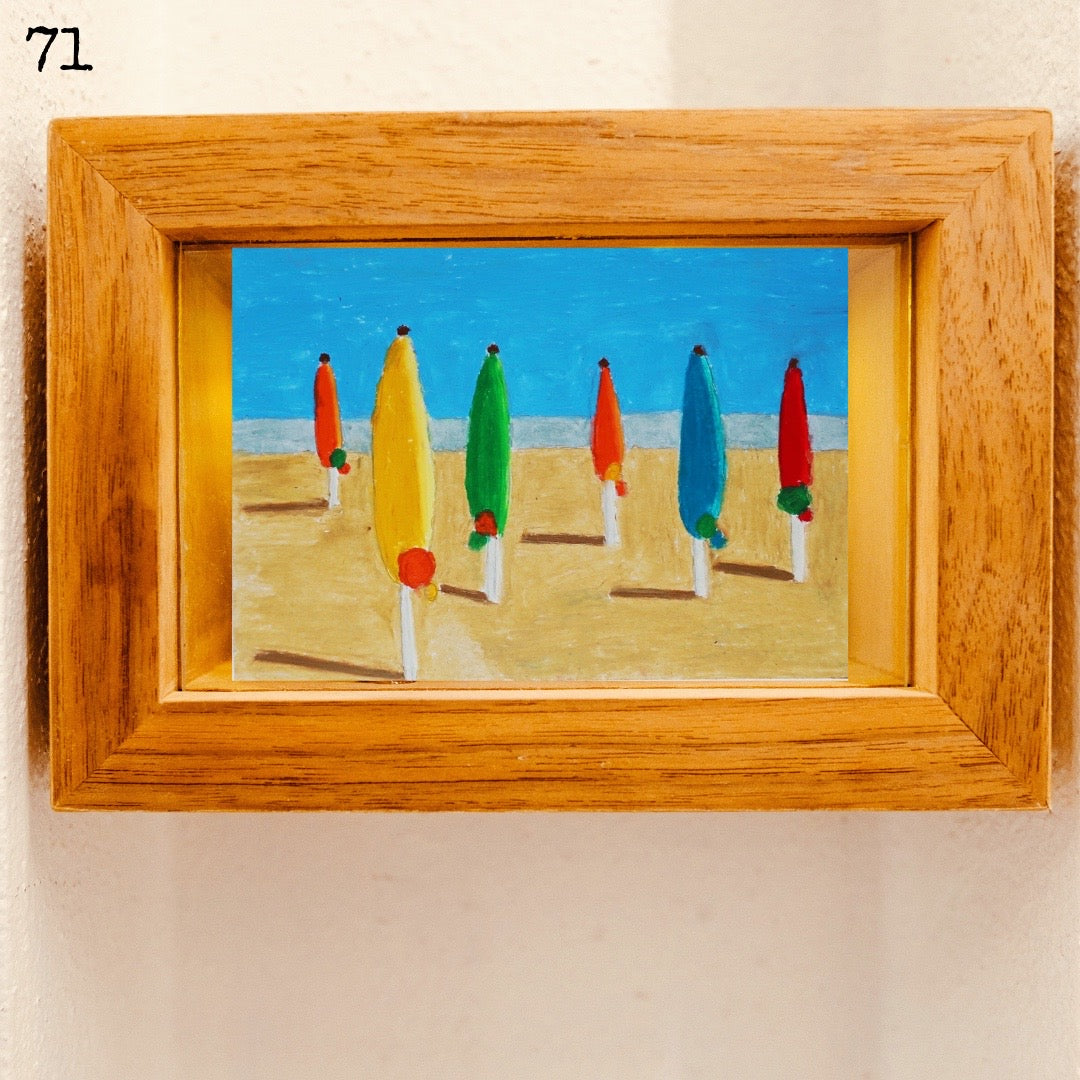 A wooden framed oil pastel painting of beach umbrellas under the blue sky