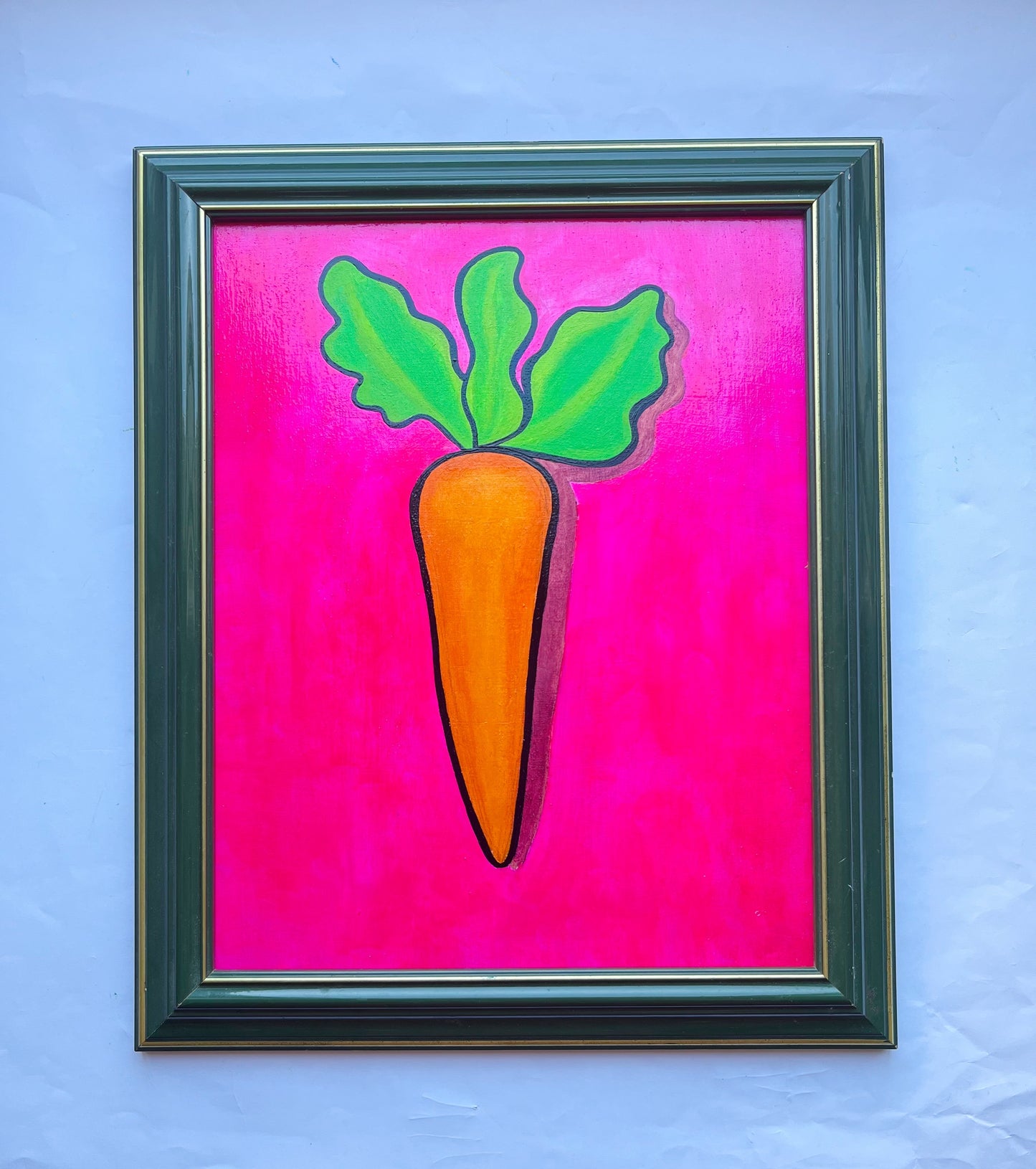 An oil painting of an orange carrot on a pink background in a thrifted frame