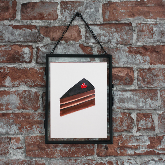 a black framed painting of a slice of chocolate cake on a brick wall