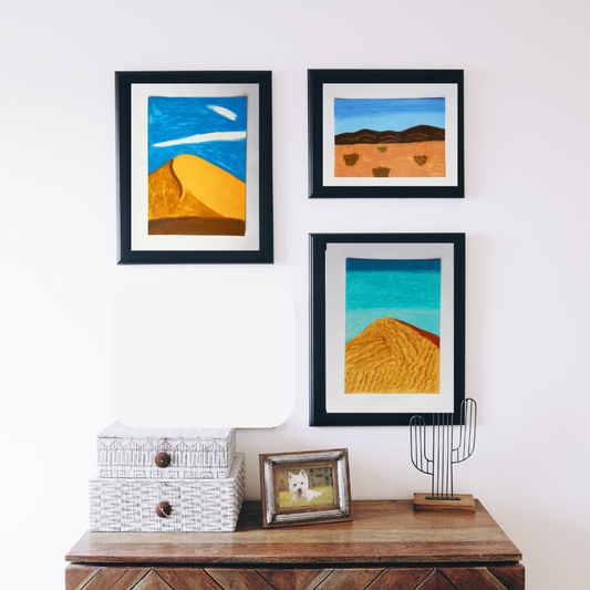 Three black framed oil pastel paintings of desert scenes