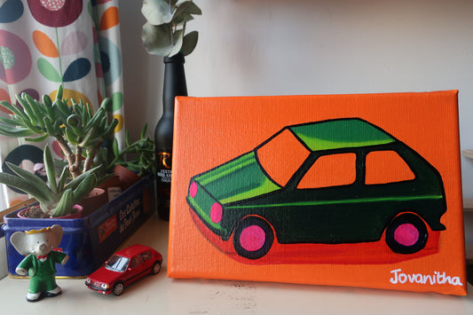 An oil painting of a green VW car against an orange background on a white shelf