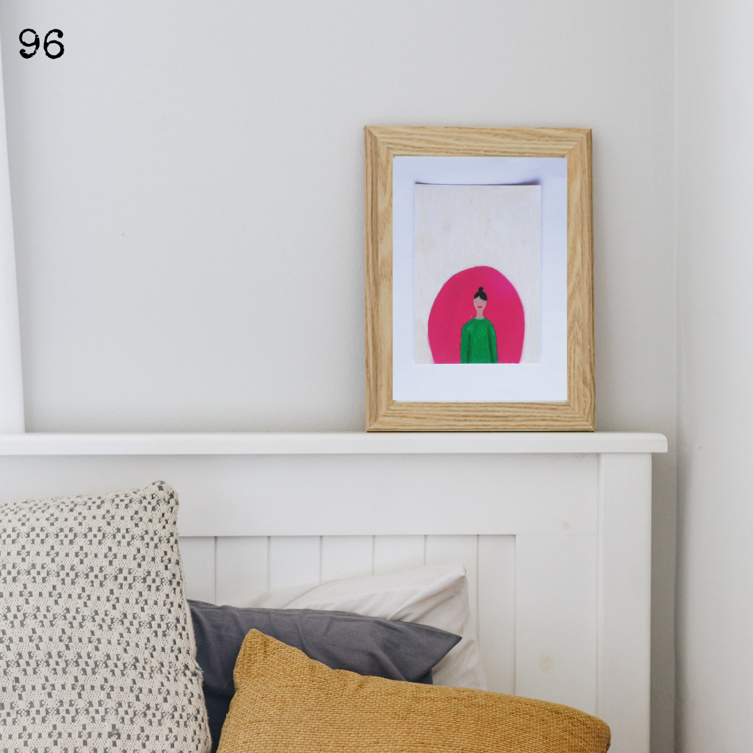A wooden framed oil pastel painting of a green lady in a pink arch on a white mantelpiece