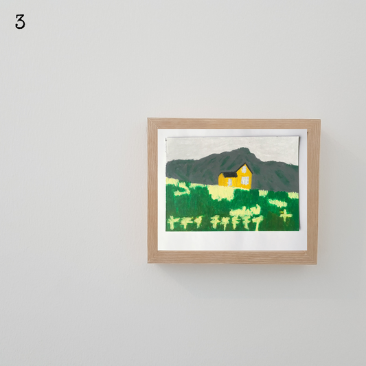 A wooden framed oil pastel painting of a yellow house against a mountain backdrop in front of a green and yellow field 