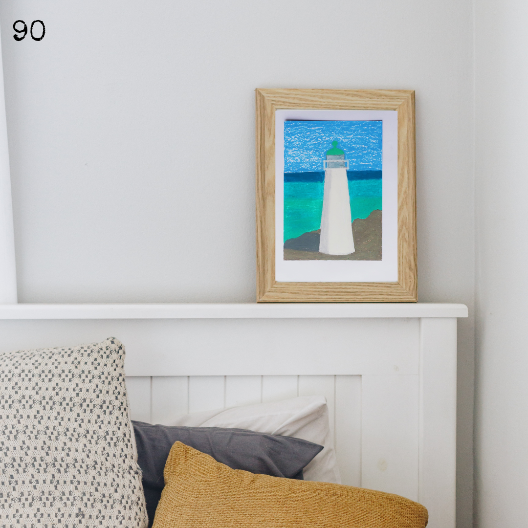 A wooden framed oil pastel painting of a white lighthouse against a blue sea