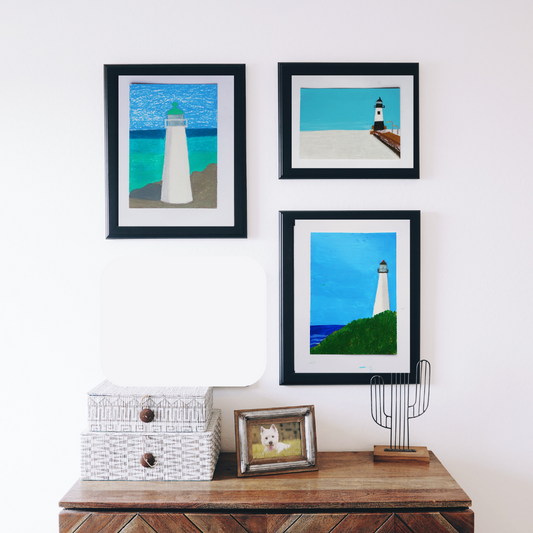 Three black framed paintings of lighthouses against the blue sky