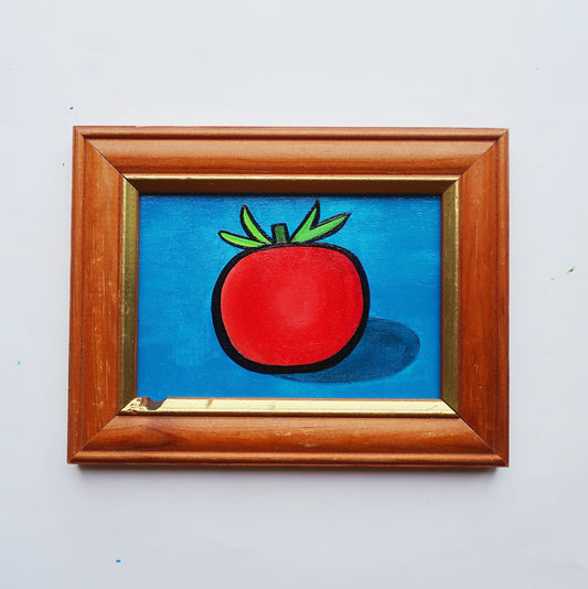 An oil painting of a red tomato on a blue background in a thrifted frame