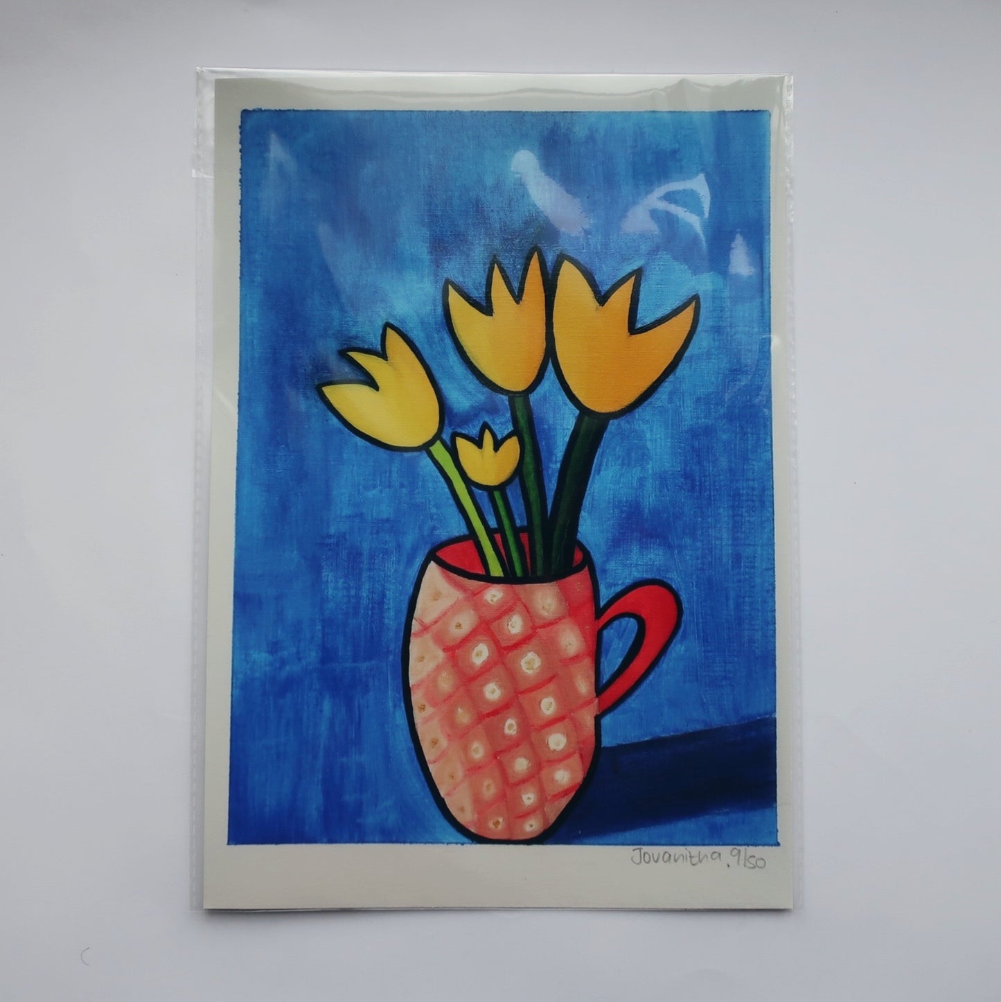 A print of an oil painting of yellow tulips in a pink mug against a blue background