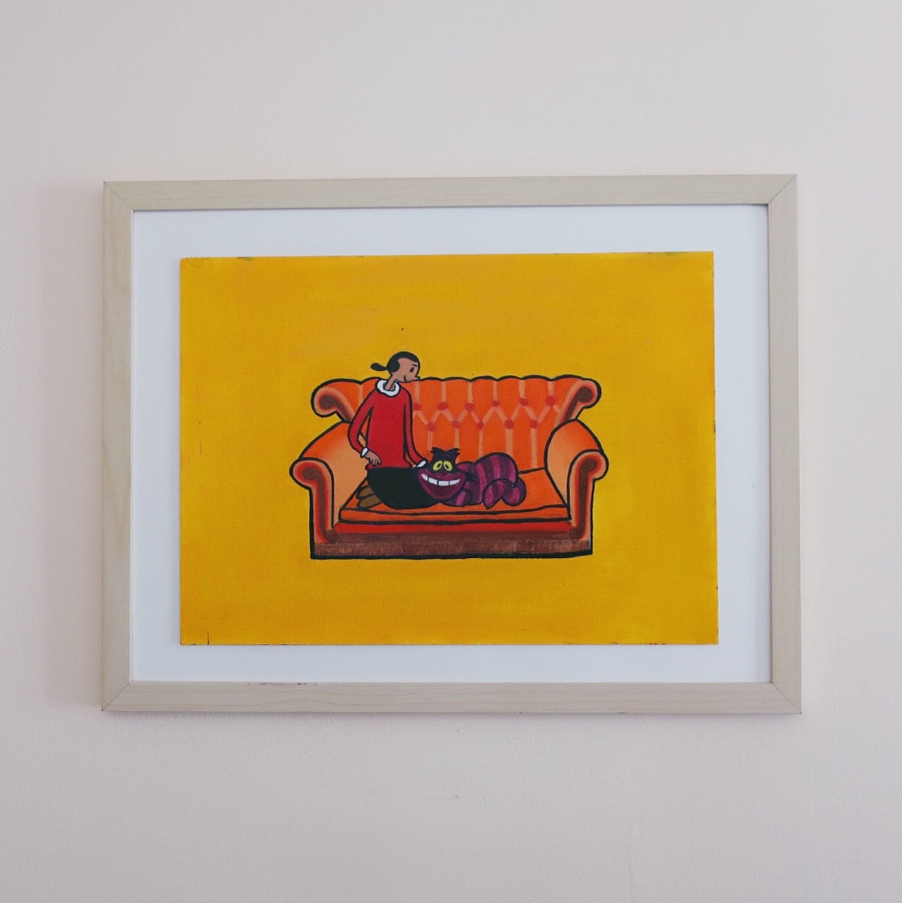 A framed oil painting of Olive Oyl sitting on Friends couch stroking the Cheshire Cat of Alice in Wonderland against a yellow background