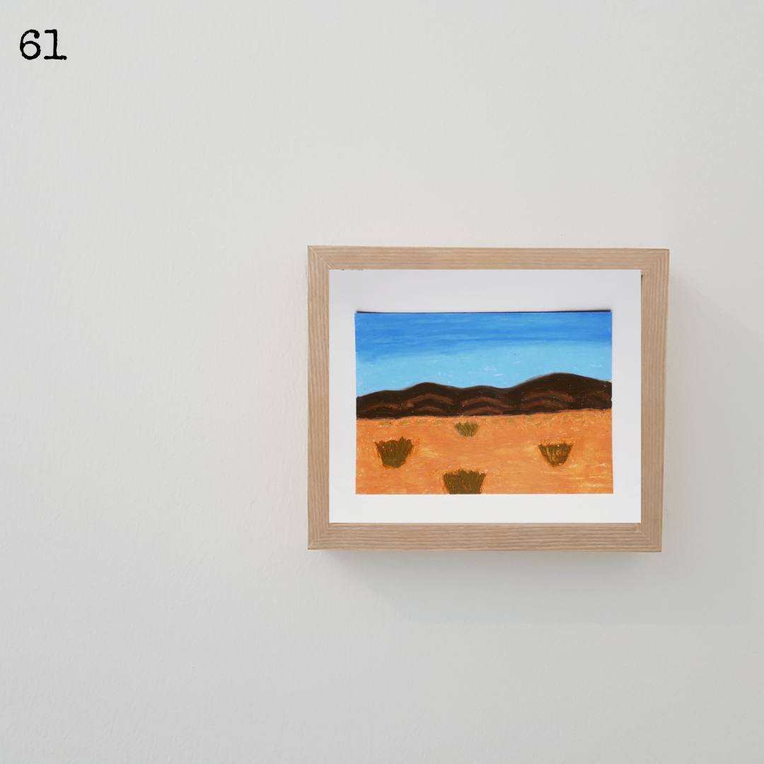 A wooden framed oil pastel painting of a desert scene with the mountain under a blue sky