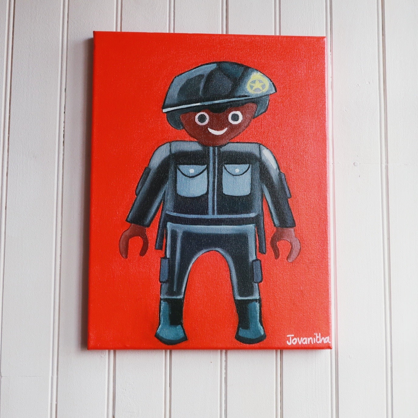 An oil painting of a black policeman Playmobil against an orange background on a white wall