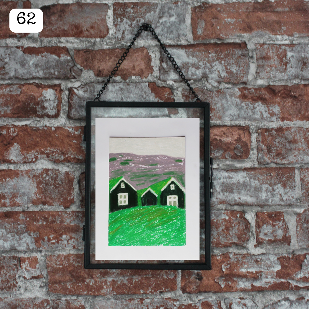 A black framed oil pastel painting of three black houses on a mountain