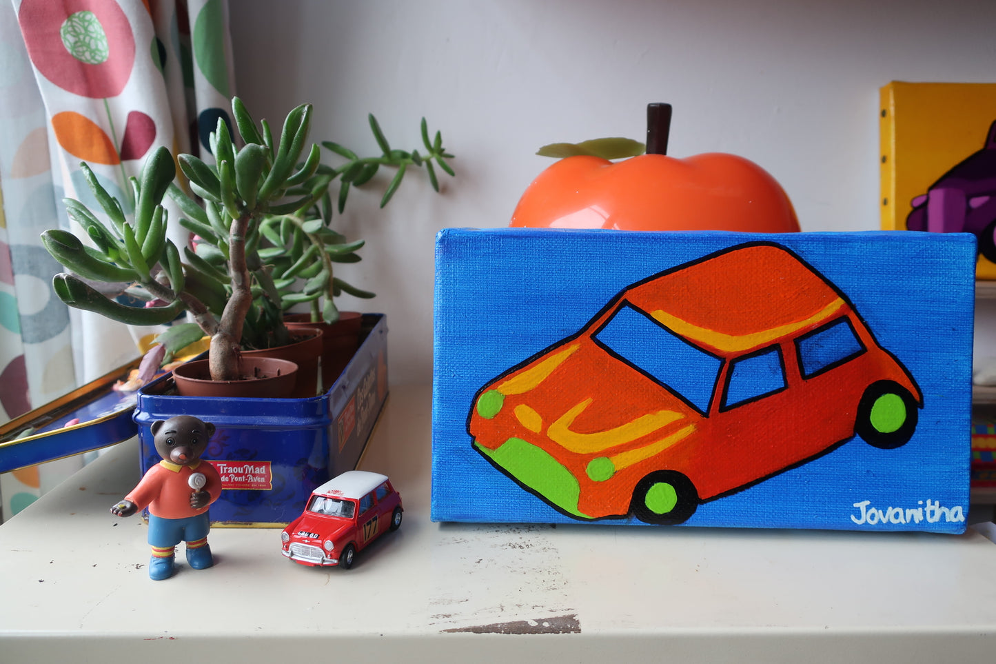 An oil painting of an orange Mini Cooper car against a blue background on a white shelf