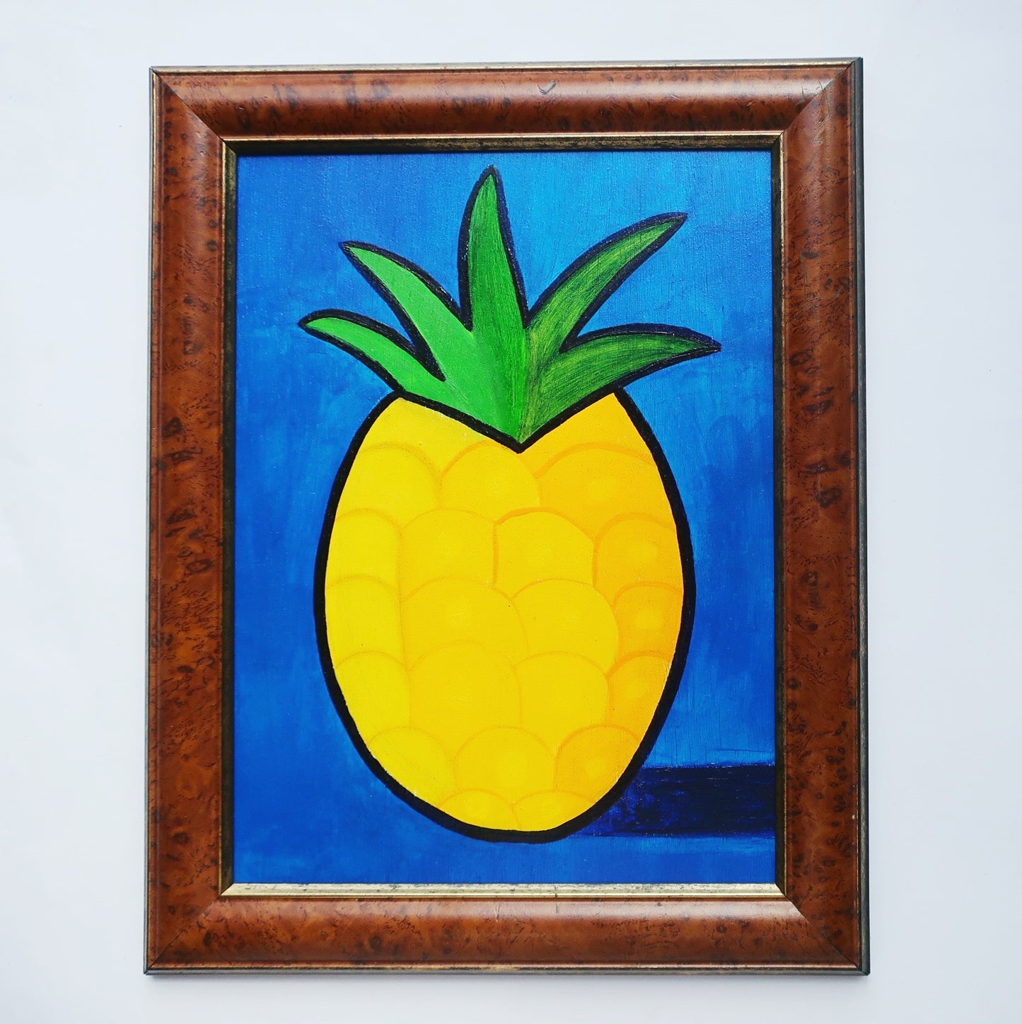 An oil painting of a yellow pineapple on a blue background in a thrifted frame