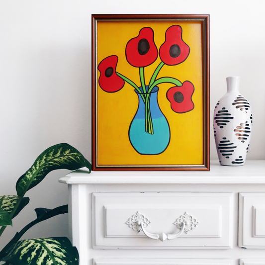 A wooden framed oil painting of four poppies in a vase on a yellow background on a white cupboard