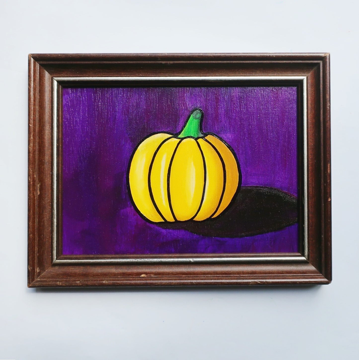 An oil painting of a yellow pumpkin on a purple background in a thrifted frame.