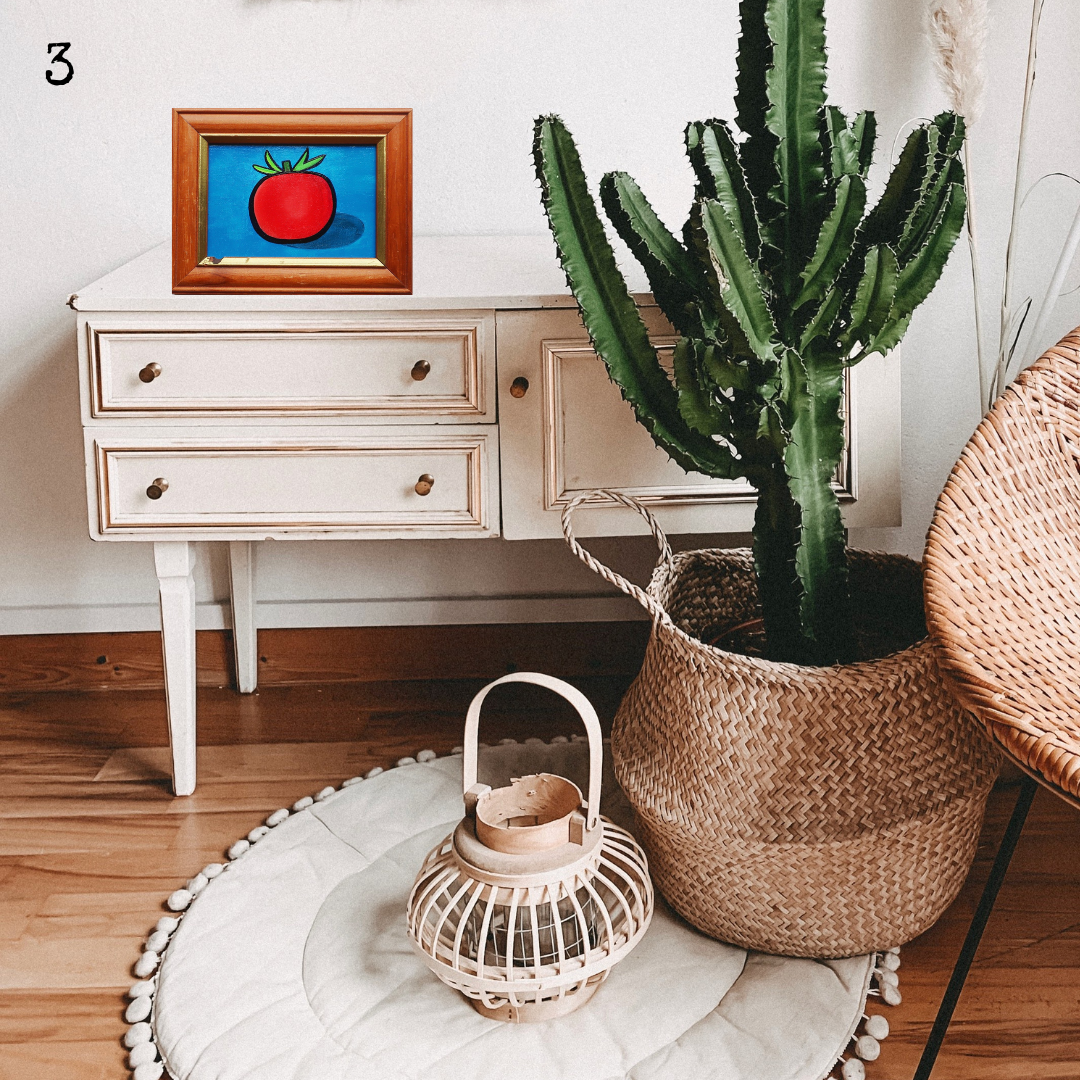 An oil painting of a red tomato on a blue background in a thrifted frame in a boho decor