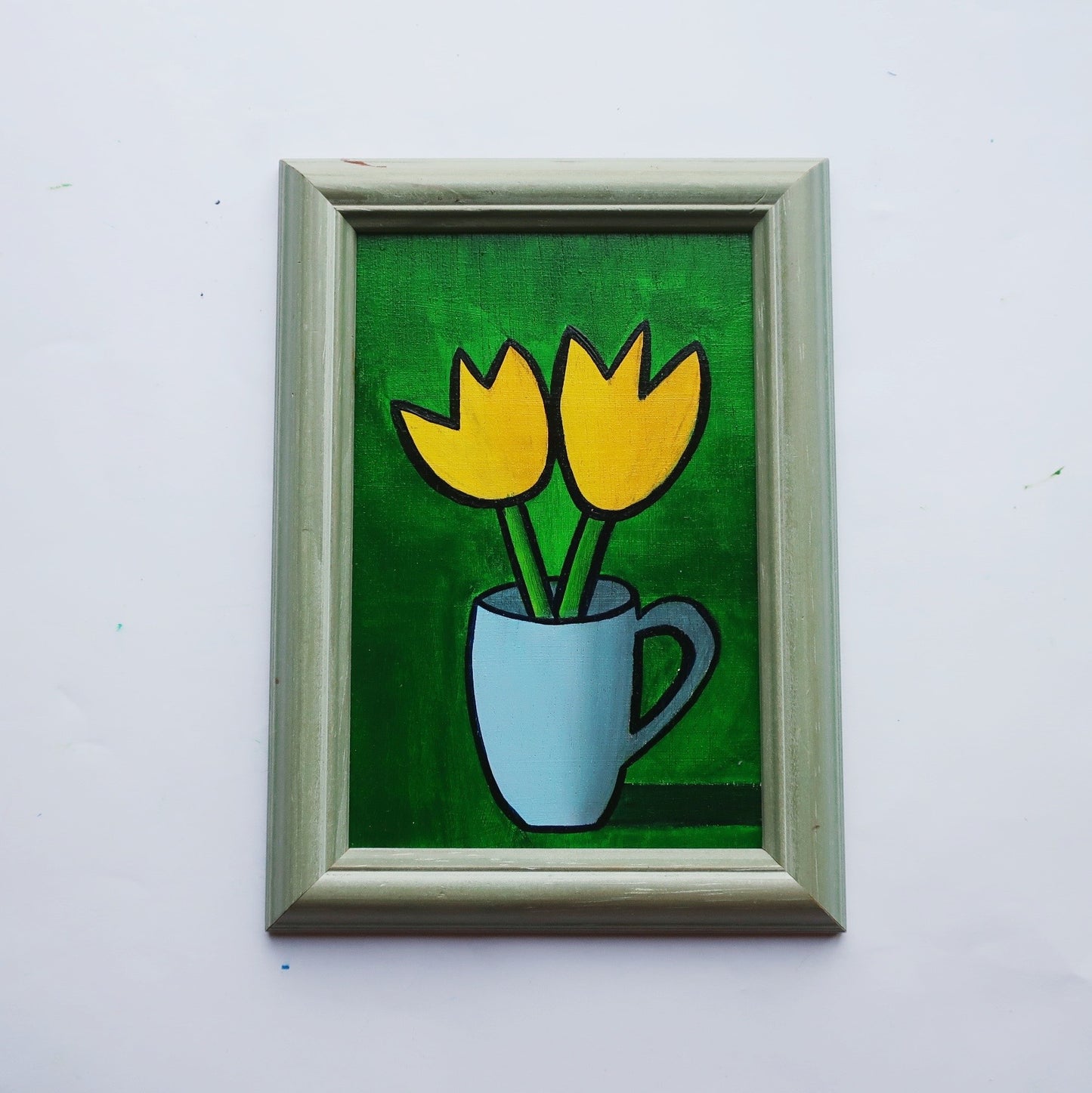 An oil painting of two yellow tulips in a blue mug on a green background in a thrifted frame